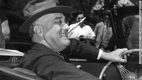 Con un cigarrillo en una boquilla apretada entre los dientes, un sonriente Franklin Delano Roosevelt se sienta alegremente al volante de su convertible, Warm Springs, Georgia, 1939. (Foto de Underwood Archives / Getty Images)