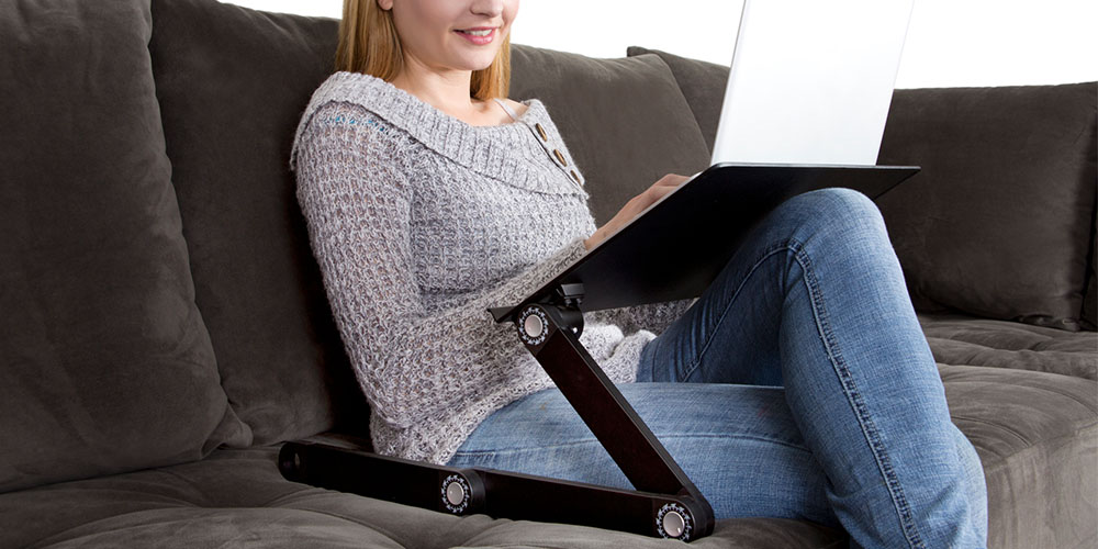Una persona que trabaja desde un sofá con un soporte para computadora portátil.